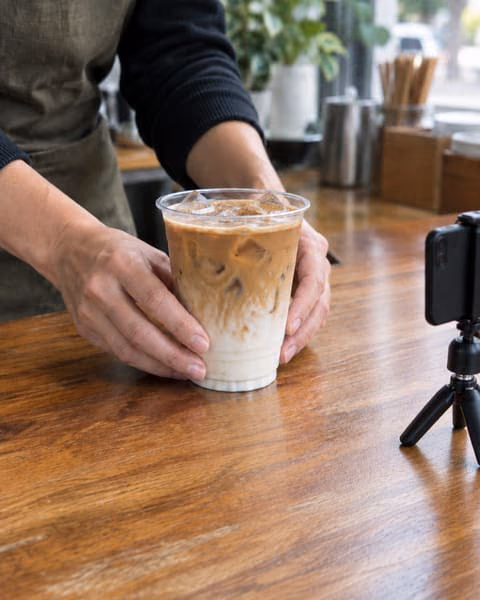 Approved work: Latte take, hands placing an iced latte on a cafe counter